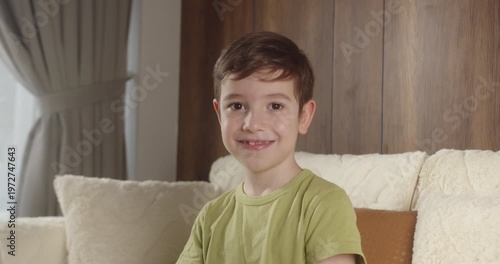 Portrait of smiling 8 year old boy with tooth gap sitting on sofa at home.