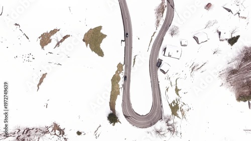 Top-down aerial view of vehicles moving through a snowy mountain hairpin curve at speed, highlighting road design and winter conditions
