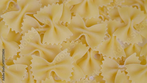 Closeup dry bowshaped pasta texture, golden farfalle pieces overlapping with serrated edges, uncooked ingredient filling frame, soft warm light, rustic kitchen pantry mood