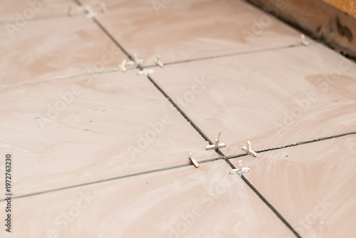 Process of laying ceramic floor tiles using plastic spacers. Close-up of beige floor tiles during installation, showing joint alignment and interior renovation work