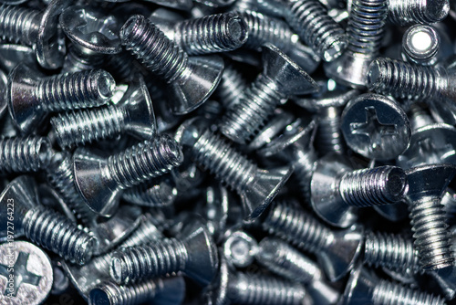 Close-up of numerous shiny galvanized countersunk screws DIN 965, their metallic luster reflecting light. An industrial, hardware background