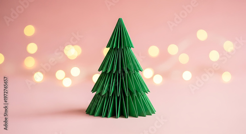 Minimalist green paper folded origami Christmas tree. Simple festive holiday craft on soft pink pastel background.