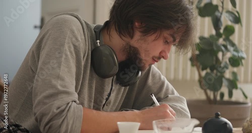 A passionate artist diligently writes and sketches while surrounded by soft sunlight in a serene space