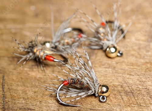 Fotografie A close-up macro shot of  handmade Fire Orange Tag euro nymph flies with gold tu