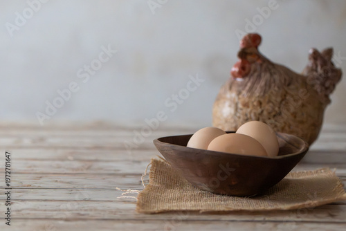 Fresh Brown Eggs in Rustic Wooden Bowl with Ceramic Hen on Distressed Wood with Copy Space