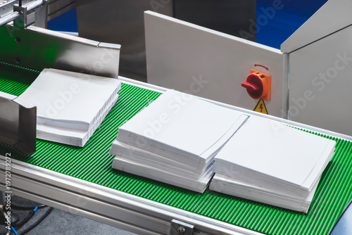 Stack of white papers is on a conveyor belt. The conveyor belt is green and the papers are piled up