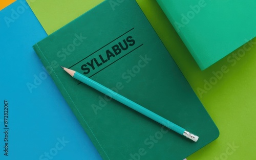 A green pencil lies on a green syllabus book on colorful background