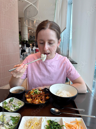Fotografie Young woman enjoying a asian meal in a modern restaurant, eating rice with chops