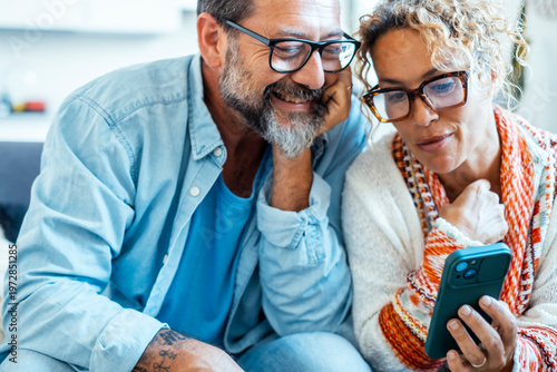 Photos Two people sitting on sofa at home enjoying smartphone content together, laughing and relaxing