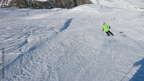 Skier in green jacket descends snowy mountain slope during sunny winter day. Slow motion POV	
