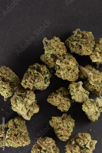 Close-up image of cannabis buds arranged on a dark surface, showcasing their green and orange hues and textured details.