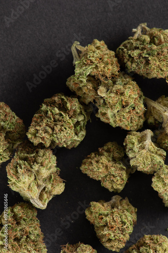 Close-up image of dried cannabis buds scattered on a black surface.