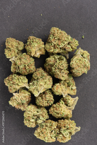 Close-up of dried cannabis buds arranged on a dark surface, showcasing their green and orange hues with visible trichomes.