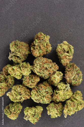 Close-up image of multiple cannabis buds arranged on a dark surface, showcasing their green and orange hues with visible trichomes.