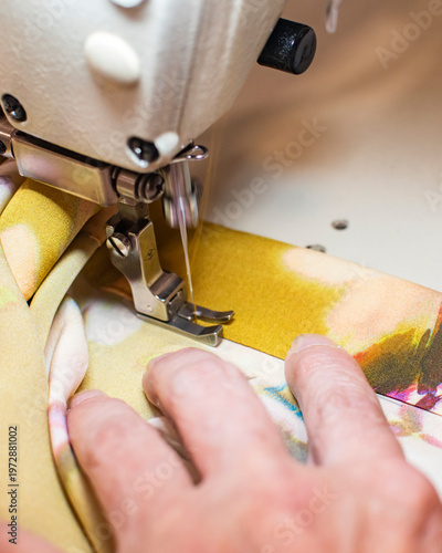 Close up of hands sewing colorful fabric on industrial sewing machine in tailoring workshop