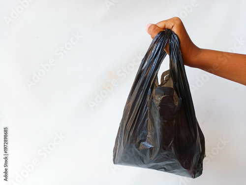 Foto Hand holding a black plastic bag against a white background, with copy space