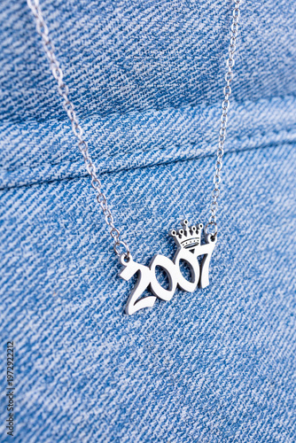 Close-up of a silver pendant featuring the year 2007 and a cute crown on a chain, set against a blue background.