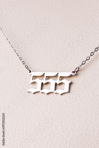 Close-up of a silver pendant with the number 555 on a chain, set against a luxurious white leather background.