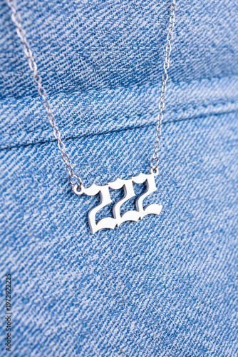 Close-up of a silver pendant with the number 222 on a chain, set against a blue background.