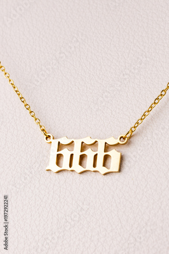 Close-up of a gold pendant with the number 666 on a chain, set against a luxurious white leather background.