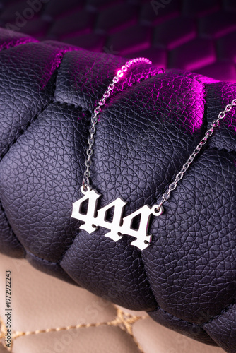 Close-up of a silver pendant with the number 444 on a chain, set against a luxurious black leather background.