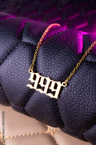 Close-up of a gold pendant with the number 999 on a chain, set against a luxurious black leather background.