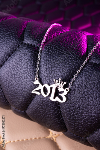 Close-up of a silver pendant with the year 2013 and a cute crown on a chain, set against a luxurious black leather background.