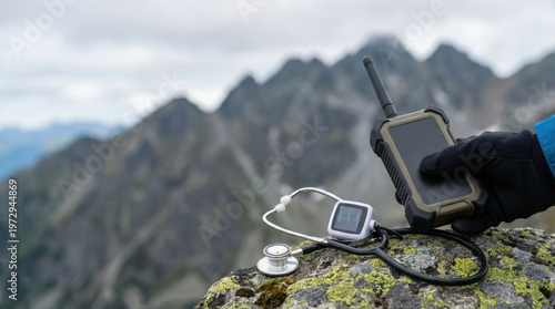Hand holding rugged satellite phone on mountain rock with stethoscope and portable heart rate monitor, outdoor medical emergency concept
