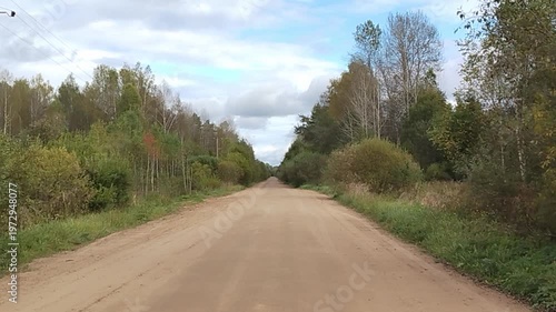 Dirt road stretches through lush greenery with trees lining both sides, under a cloudy sky, showcasing the serene landscape of a rural area in Eastern Europe