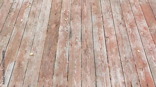 Wooden deck surface with weathered planks and scattered leaves, showcasing the natural texture and color variations in a serene outdoor setting