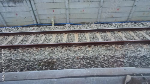 Video of a view of a rusty train track with gravel and rail sleepers from the POV of a passenger sitting on a moving train. Footage of the track for the train's wheels to run steadily, safely, and eff