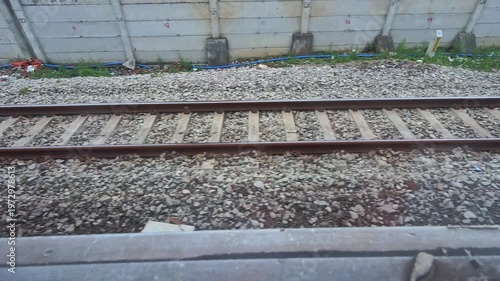 Video of a view of a rusty train track with gravel and rail sleepers from the POV of a passenger sitting on a moving train. Footage of the track for the train's wheels to run steadily, safely, and eff