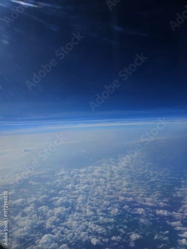 High-altitude aerial shot from a flight over Andaman, revealing the earth's atmosphere transitioning from deep blue to scattered white clouds below.