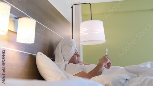 Man with a towel texting in bed on smartphone