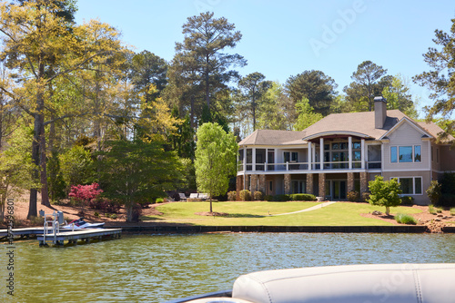 Foto A beautiful two-story contemporary lake house with a dock and lush green lawn on