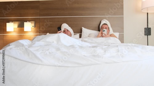 Couple in bed using phone and watching tv