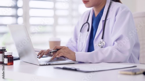 Asian adult female doctor professional using laptop computer for patient care medical records online consultation at clinic office modern healthcare setting
