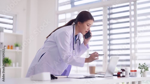 Asian medical professional adult woman busy consult patients using mobile phone laptop managing health records modern hospital clinic office multitasking healthcare worker technology