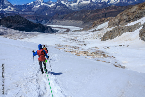 Mountaineers in rope team with crampons descending towards mountain hut Monte Rosa Hut and glacier Grenzgletscher panorama in Pennine Alps, Switzerland