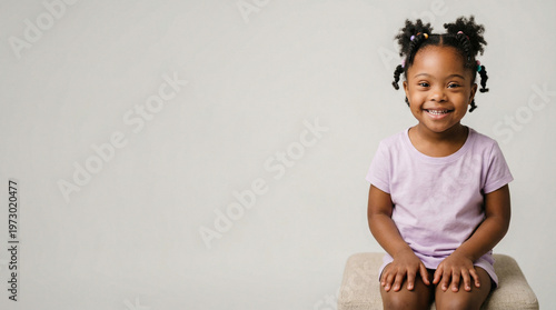Smiling young Black girl with braids sitting in a studio, friendly expression and casual outfit, joyful childhood, sweet lifestyle, happy portrait.