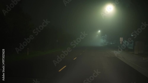 Driving along empty foggy night street with streetlights, forward motion along the road through dense fog creates atmosphere of night travel low visibility and quiet urban driving