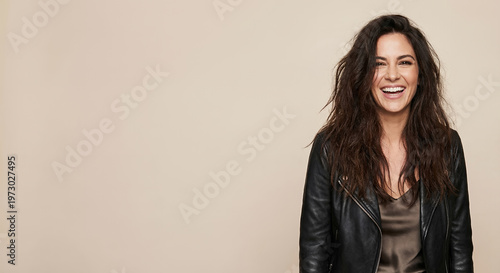 A woman with long, dark, wavy hair and a black leather jacket smiles broadly at the camera.