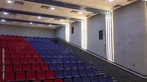 Wide Angle View of Large Seminar Hall with Red and Blue Seating Rows and Exit Door India.
