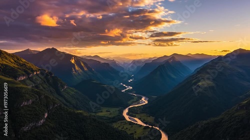 Wide aerial view of a winding river flowing through a deep mountain valley during sunset with golden hour light rays illuminating layered peaks and verdant alpine ridges.