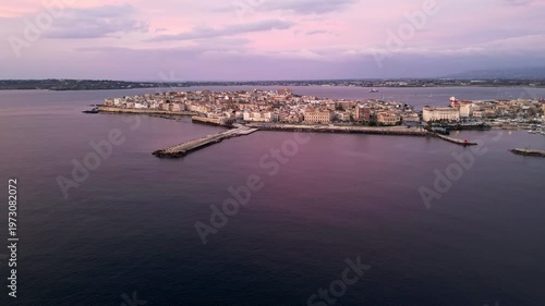 Aerial view of Ortigia at dawn, showcasing the tranquil waters, historic buildings, and the harbor with boats, creating a serene coastal landscape