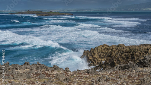 The ocean waves are raging in the strait between the small islands. White foam on blue water. Splashes on the volcanic rocks of the coast. Mauritius. Île aux Fouquets. Prison Island
 