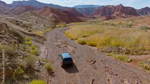 Dark station wagon navigates dirt road through eroded sandstone Konorchek canyon in Kyrgyzstan. Following drone view.