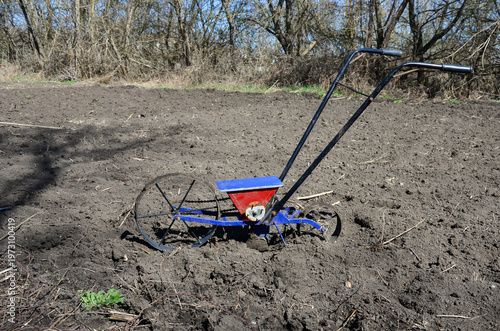 Manual two-wheel single-row precision seeder on prepared soil in a field. Manual vegetable planter on a tilled farm land, spring planting season.