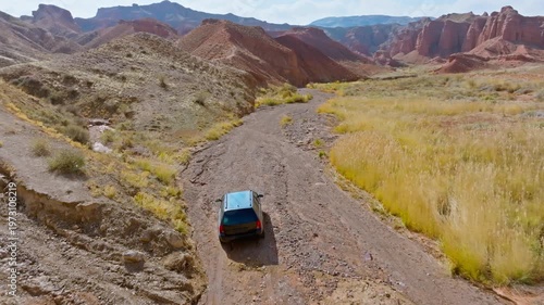 Car navigates a dry river bed through eroded sandstone mountains in Konorchek canyons, Kyrgyzstan. Following drone view.