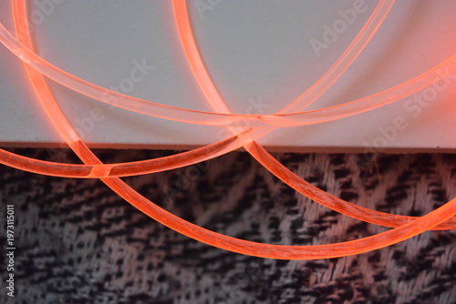 Tableau sur toile Beautiful unusual plastic tube with soft orange lighting, transparent wires, light guides, LED lighting fixtures located on a white plastic background in daylight